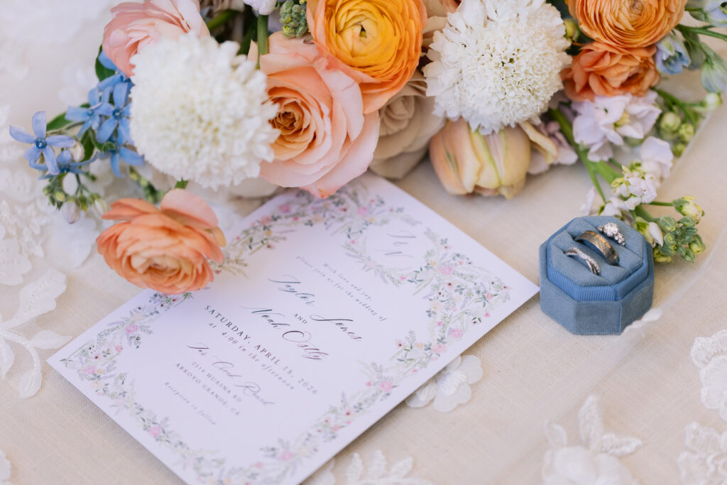 invitation suite alongside spring floral arrangement and wedding rings