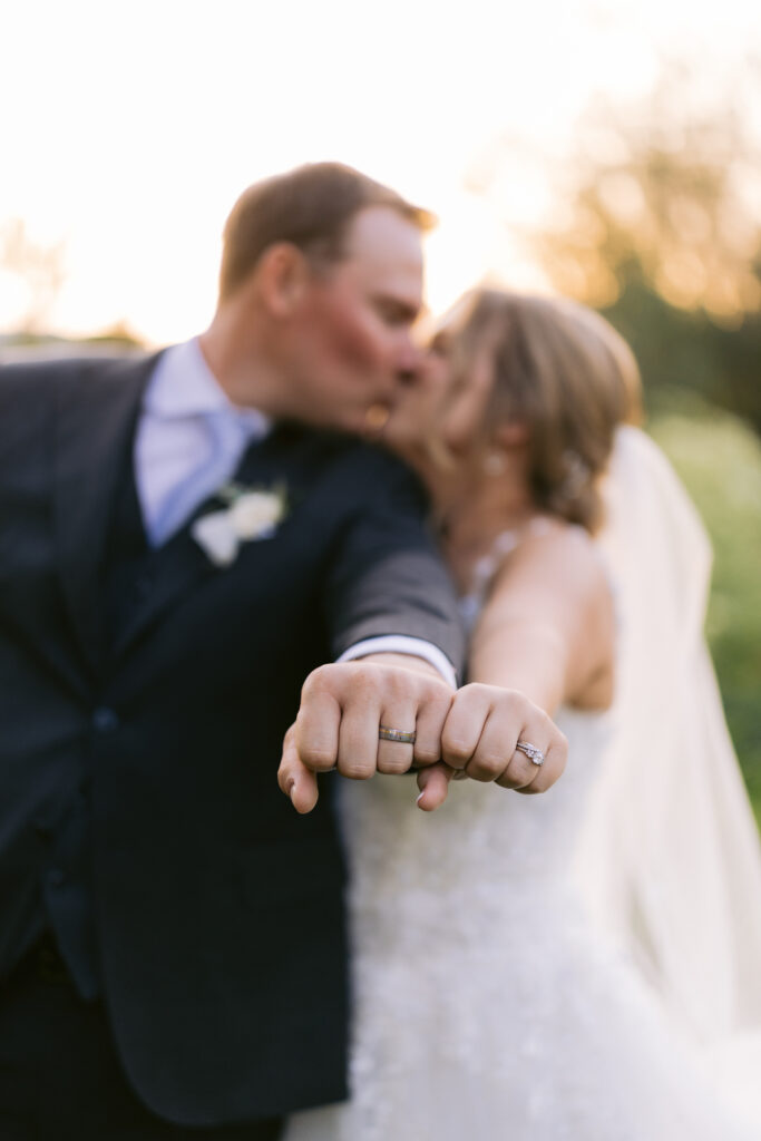 bride and groom show off wedding rings and kiss